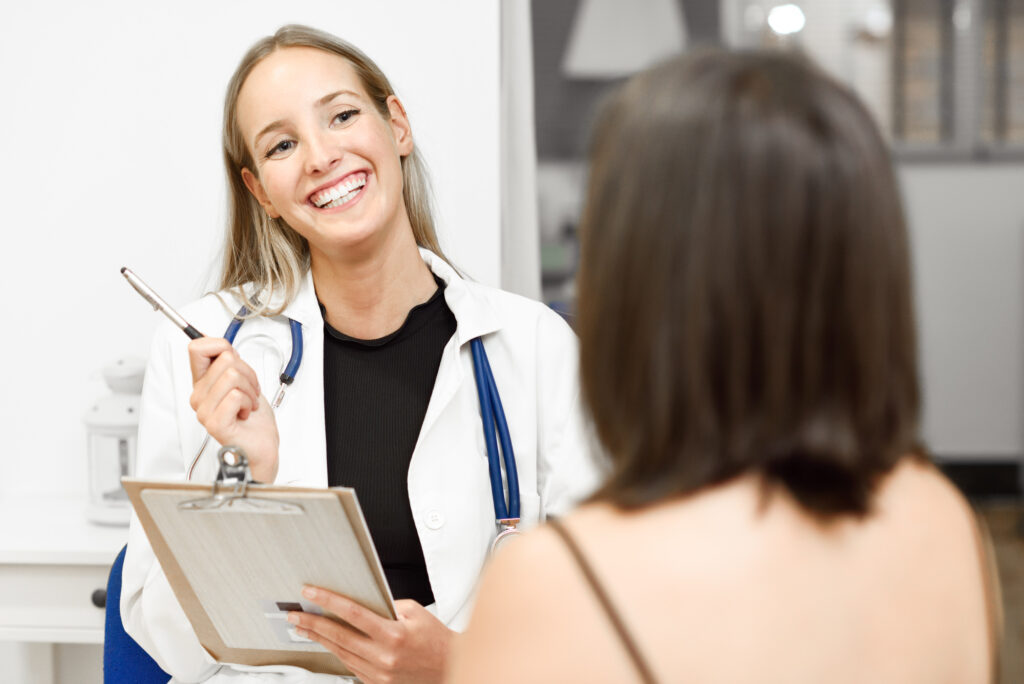 Smiling female doctor with a clipboard explaining family planning near Plano to her patient, a brunette woman facing away.