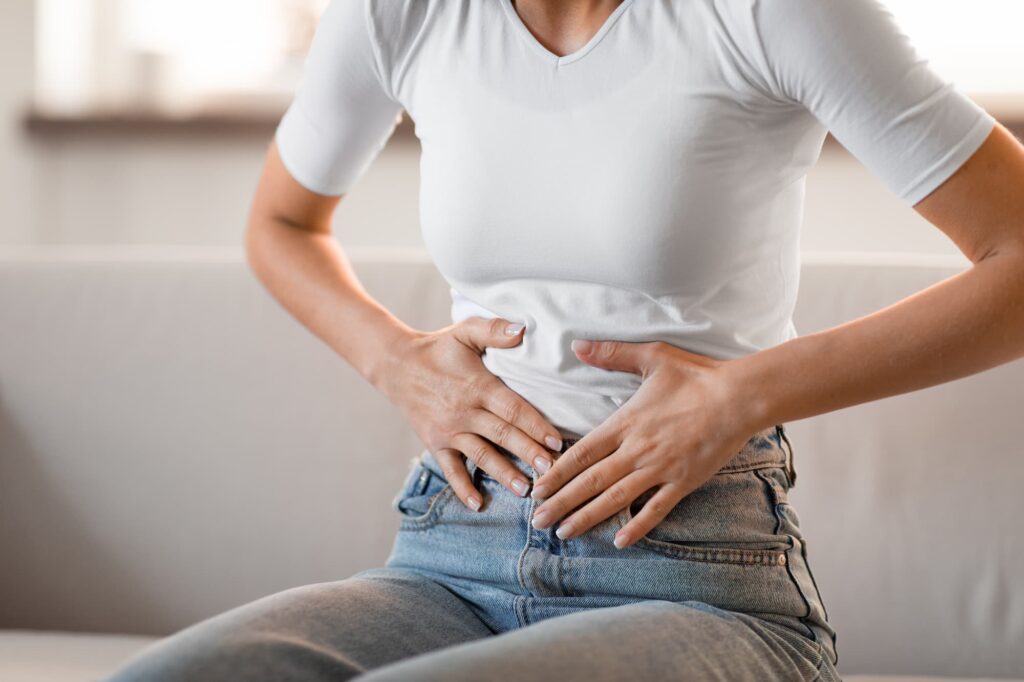 Woman pressing her hands to her lower abdomen as she struggles with pelvic discomfort near Plano.