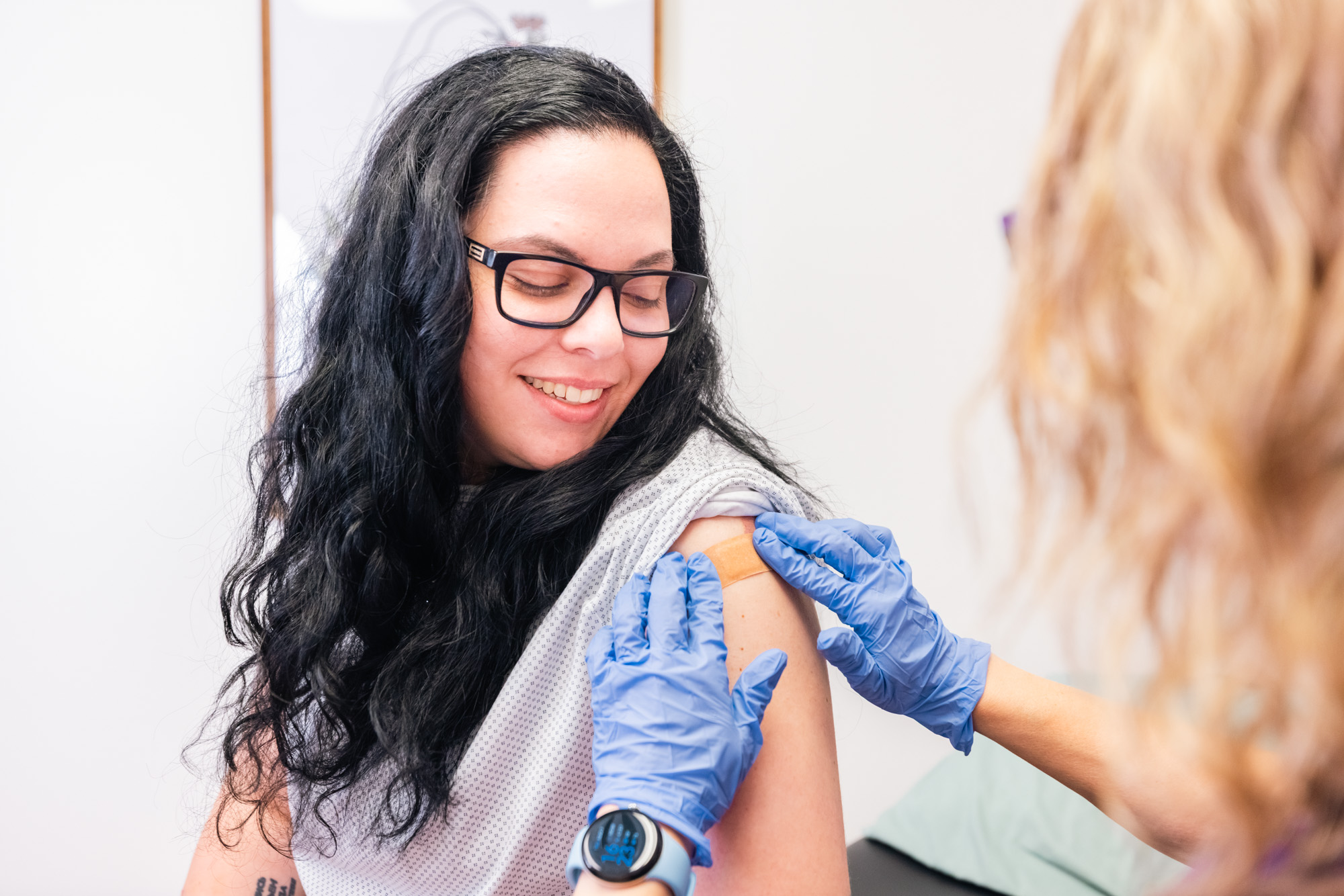 A gloved medical provider adheres a bandage to a woman's shoulder after administering GLP-1 in Frisco.